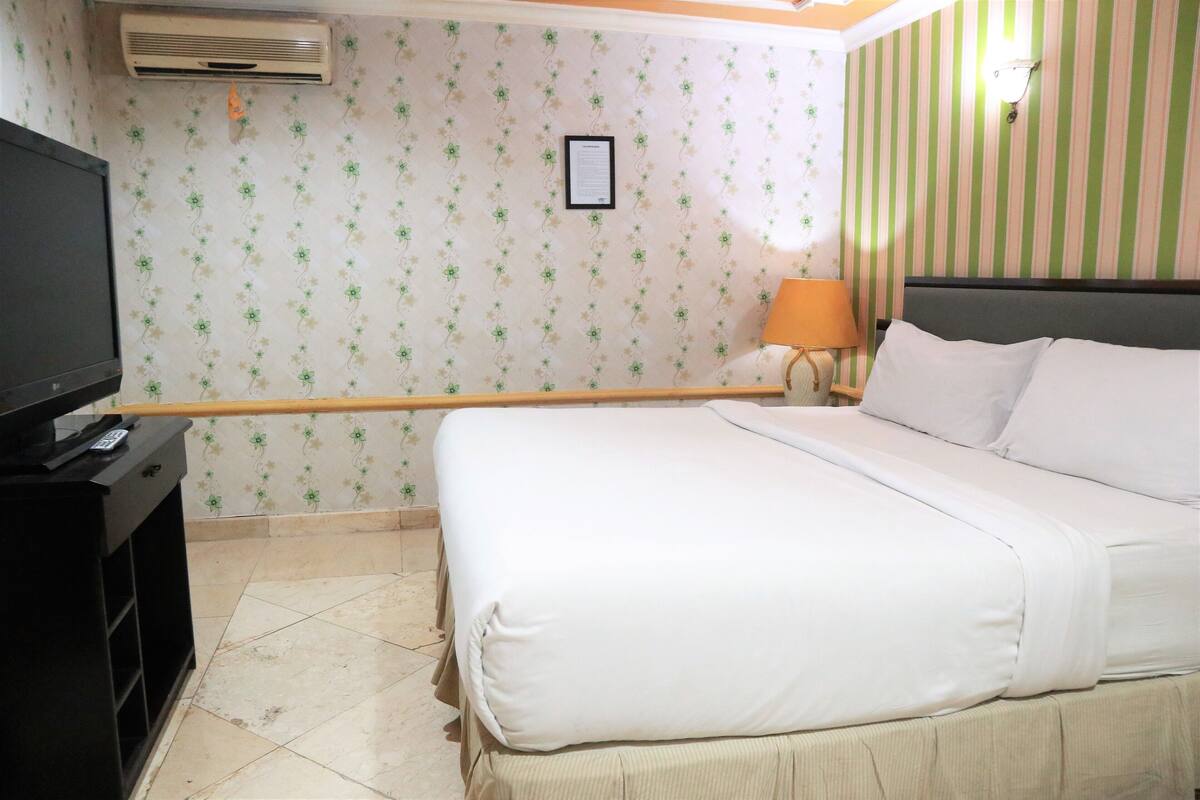 A hotel room with a bed, a TV, a lamp, and a wall with striped wallpaper.