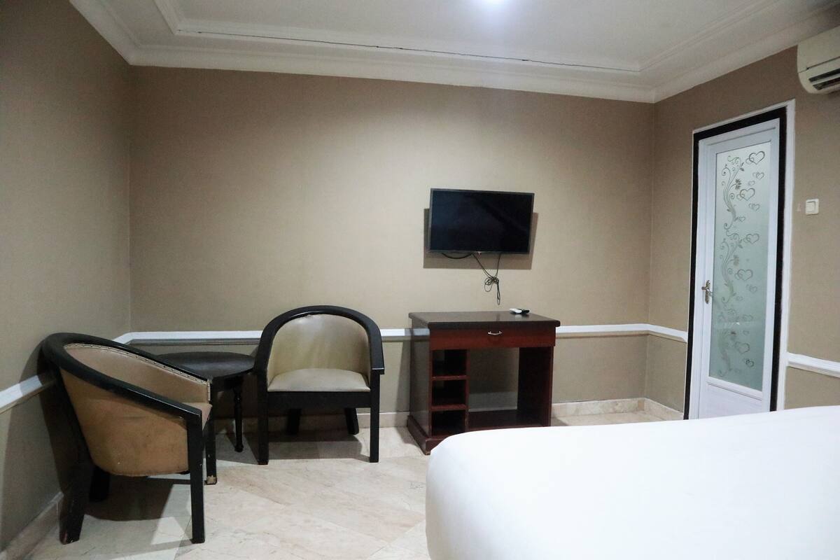 A hotel room with a bed, a desk with a chair, a television, and a door with a decorative glass panel.