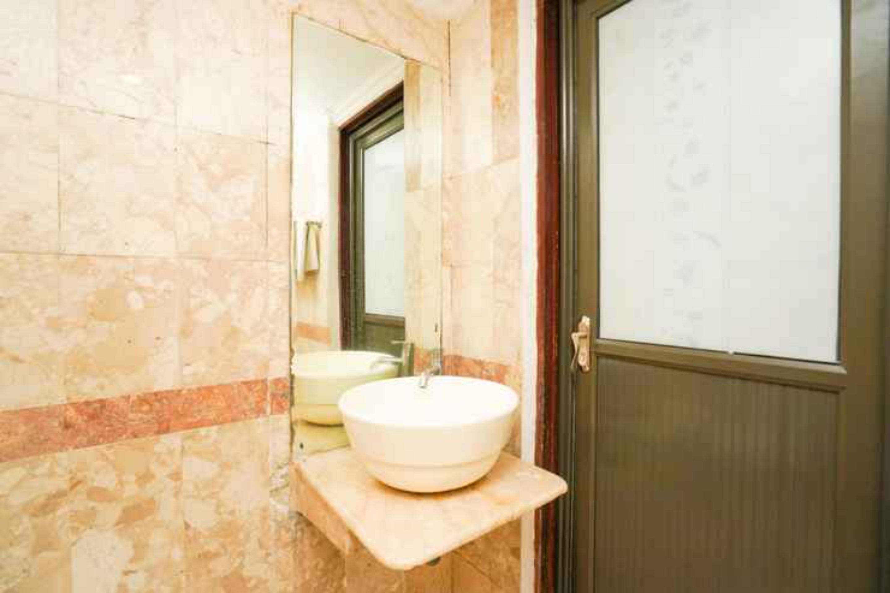Un baño con pared de mármol, un lavabo blanco y una puerta de madera.