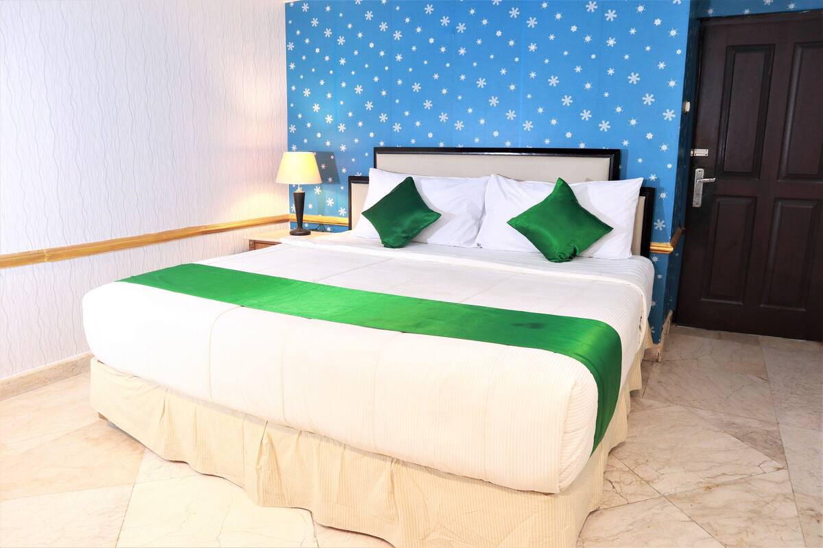 A neatly made bed with a green and white bedspread, a headboard with a blue wall featuring white snowflake patterns, and a wooden floor.