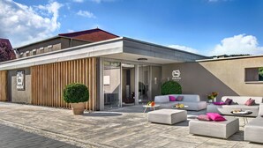 Un área de estar al aire libre, moderna, con sofá y sillones, una planta en maceta y una mesa de comedor para dos personas.
