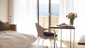 Un dormitorio con cama, una silla, una mesa con un florero y vistas al exterior a través de un amplio ventanal.