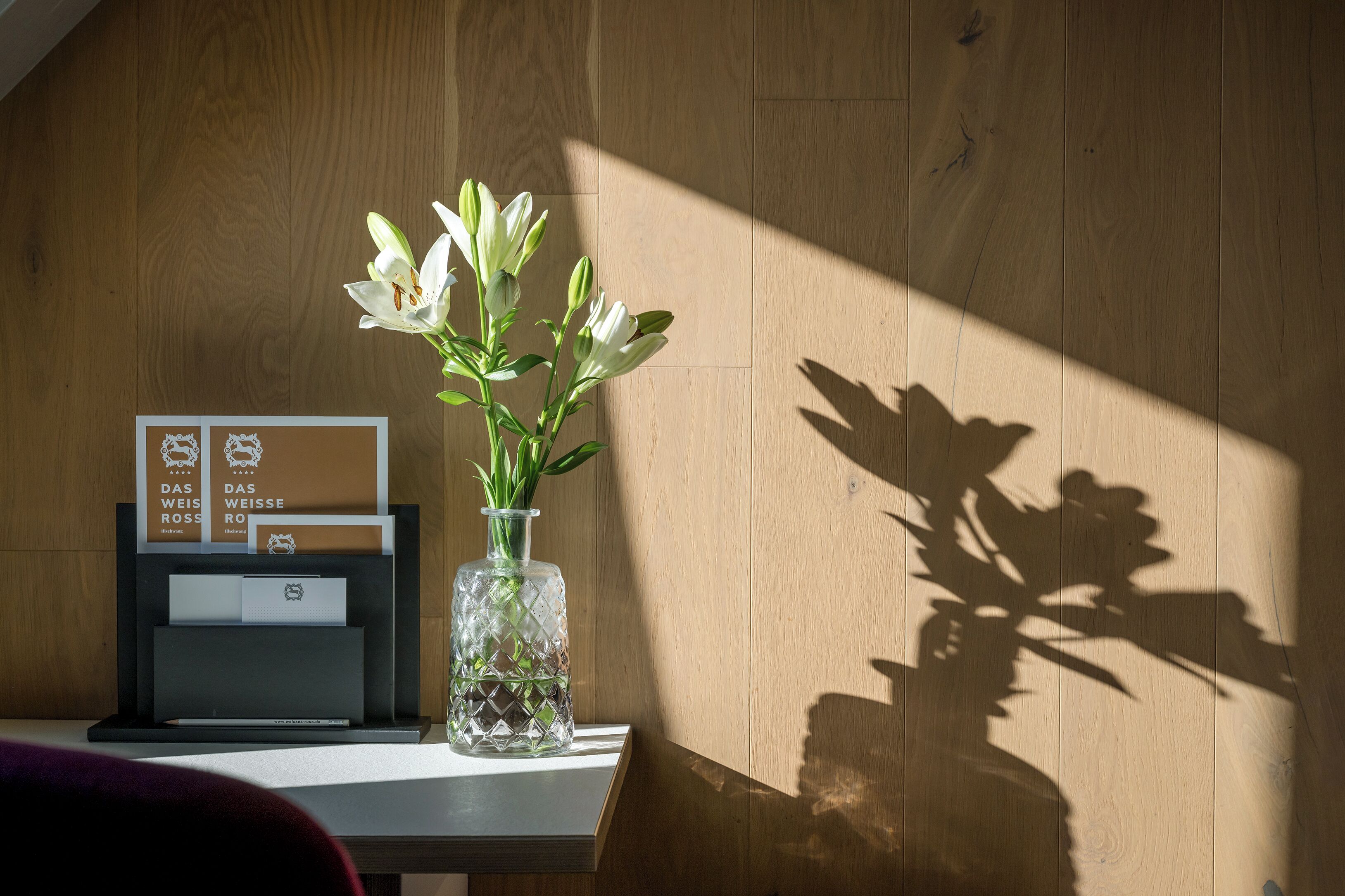 A wooden wall with a glass vase containing white flowers on a table.