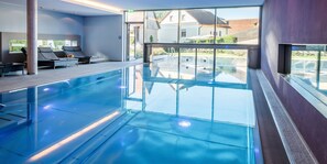 An indoor swimming pool with clear glass walls, lounge chairs, and a view of the outside. - Landhotel Weißes Roß (Illschwang)