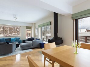 A modern living room with a sofa, a dining table, and a large window with a view of a snowy landscape. - Kita Kitsune Chalet (Kutchan)