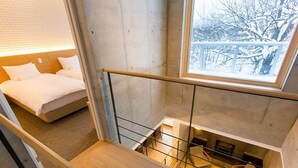 A modern hotel room with a bed, a wooden desk, and a view of a snowy outdoor scene through a window. - Mizunara Chalet (Kutchan)