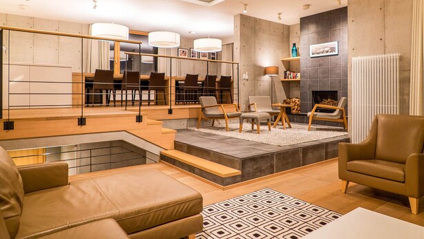 A modern living room with a dining area, a fireplace, and a staircase leading to an upper level. - Mizunara Chalet (Kutchan)