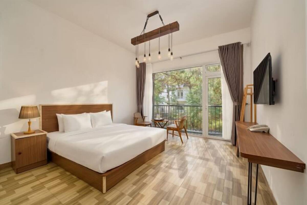 A hotel room with a large bed, a desk, a chair, a TV, and a balcony with a view.