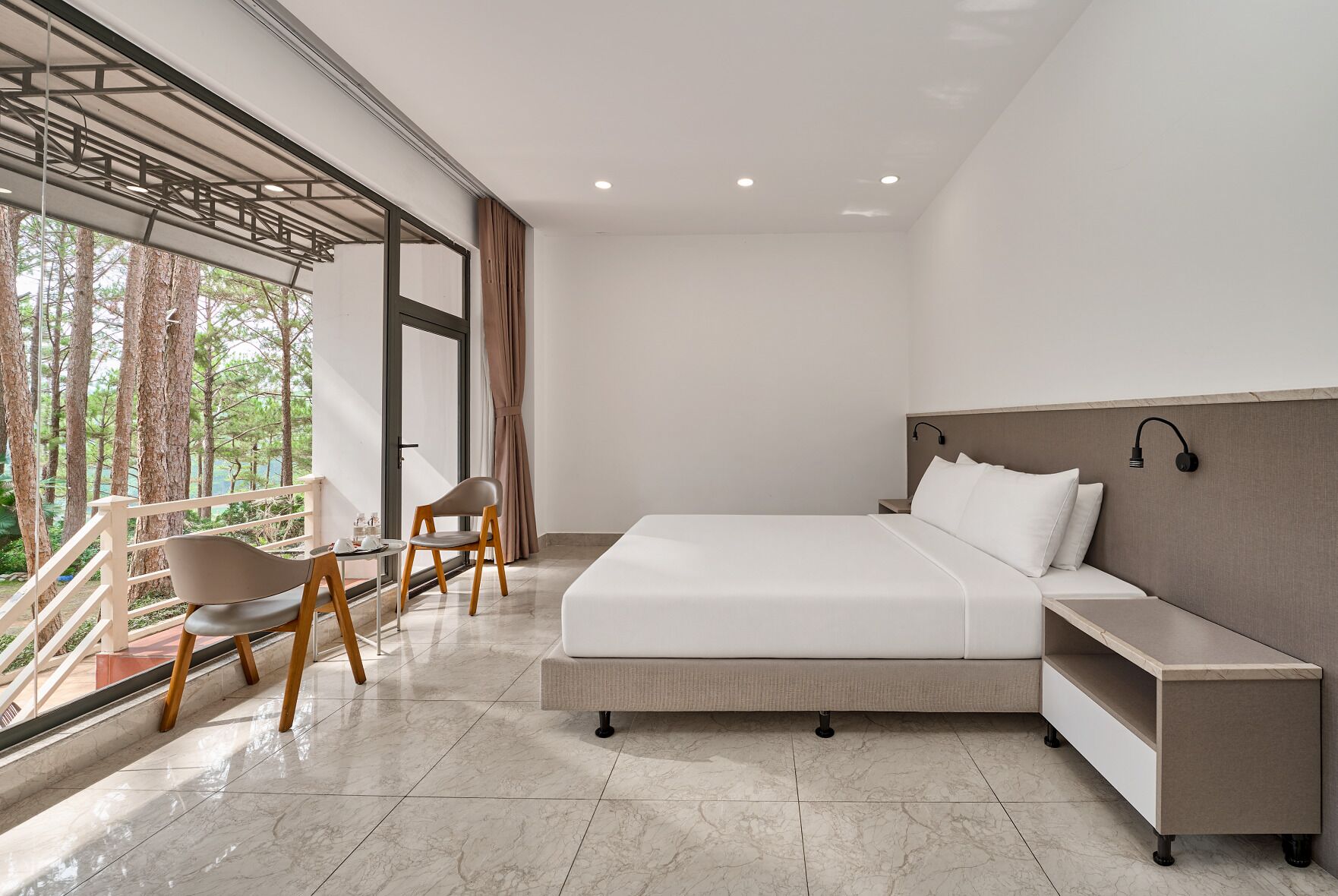 Une chambre moderne avec un grand lit, une table de chevet, une chaise et un balcon donnant sur la forêt.