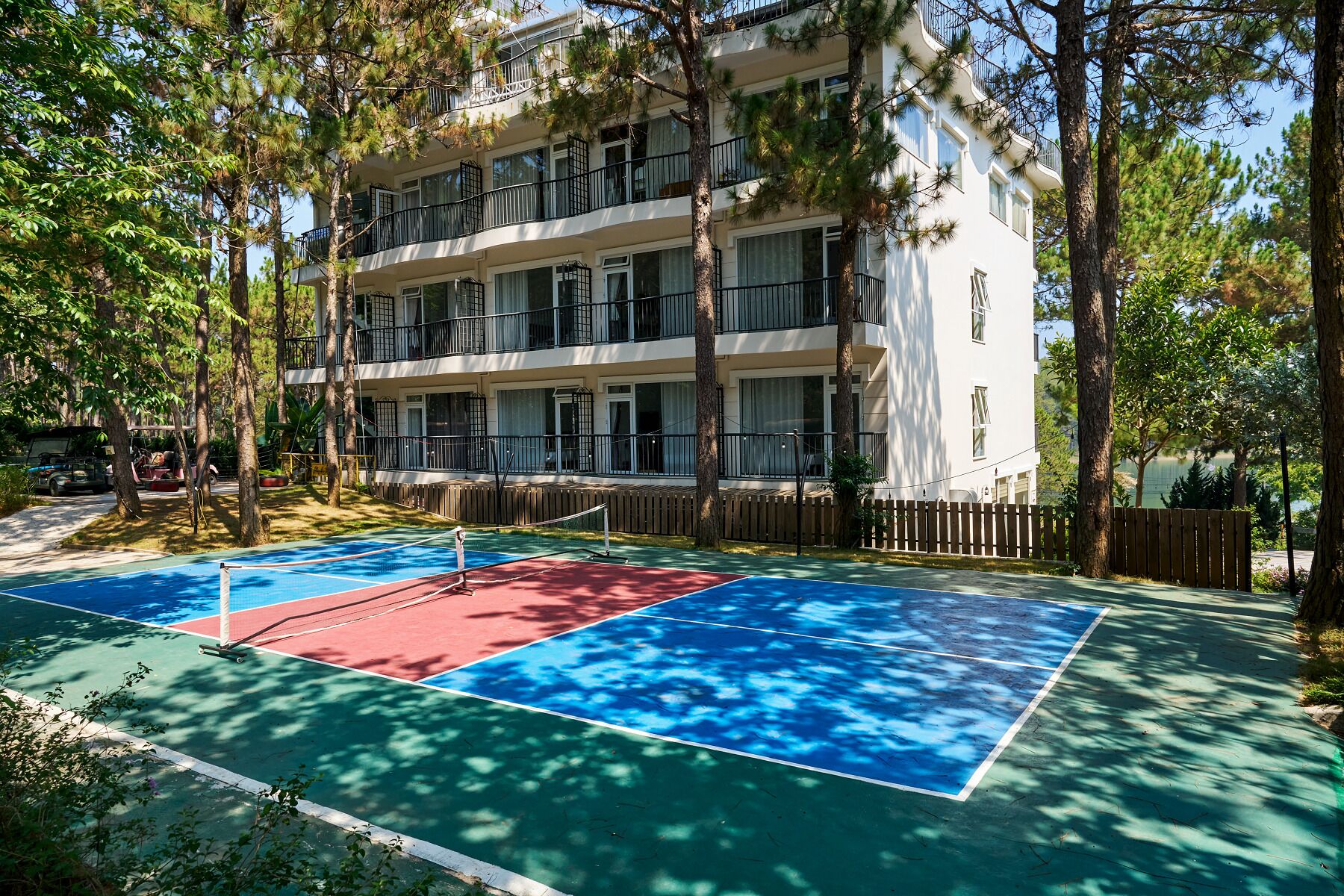 A multi-story building with balconies, a tennis court, and surrounding trees.