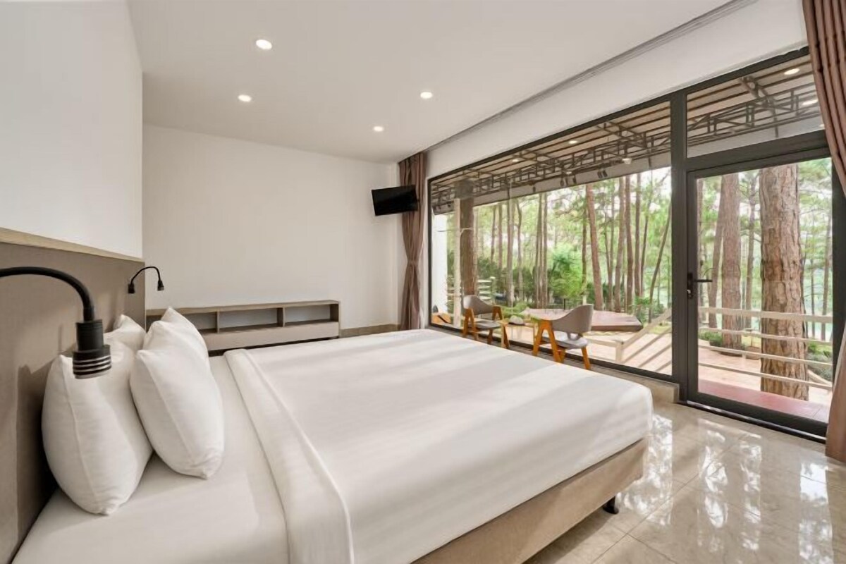 A modern bedroom with a large bed, a TV, and a view of a forest through a glass door.