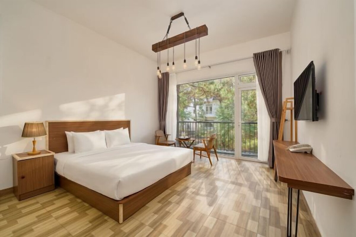 A hotel room with a large bed, a desk, a chair, a TV, and a balcony with a view.