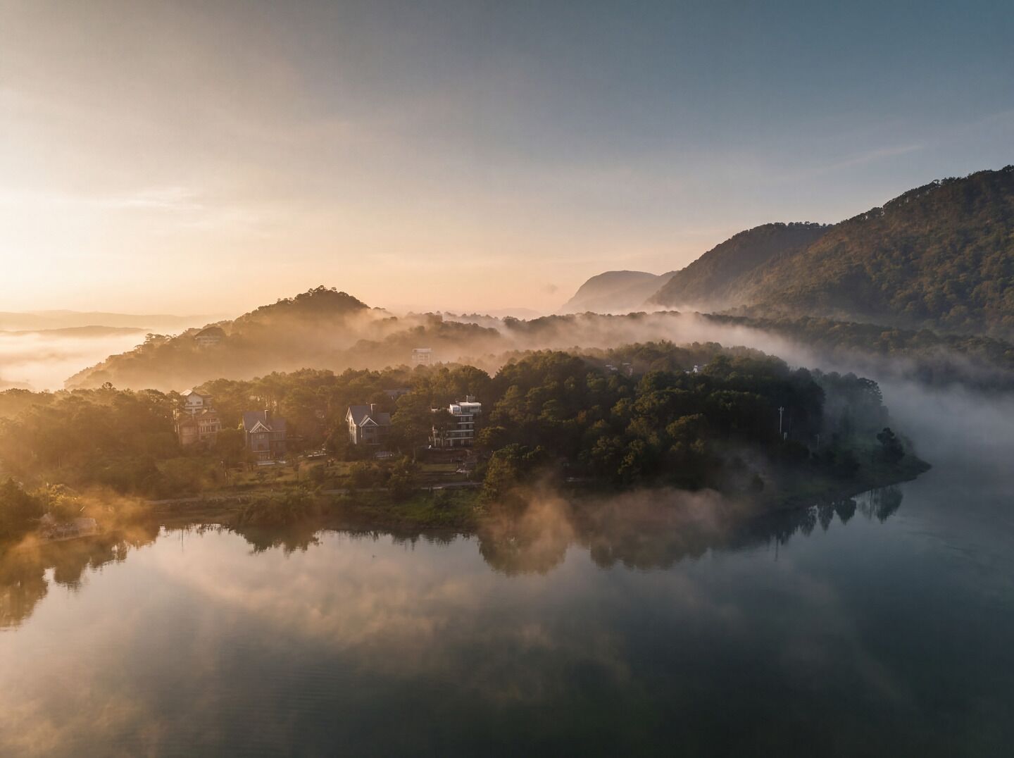 A serene lakeside village with houses nestled among hills, surrounded by mist.