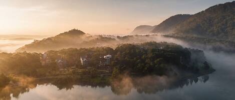 A serene lakeside village with houses nestled among hills, surrounded by mist.