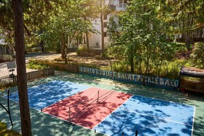 An outdoor tennis court with a red and blue surface, surrounded by trees and a wall with graffiti. - Romeo Juliet Dalat Resort (Da Lat)