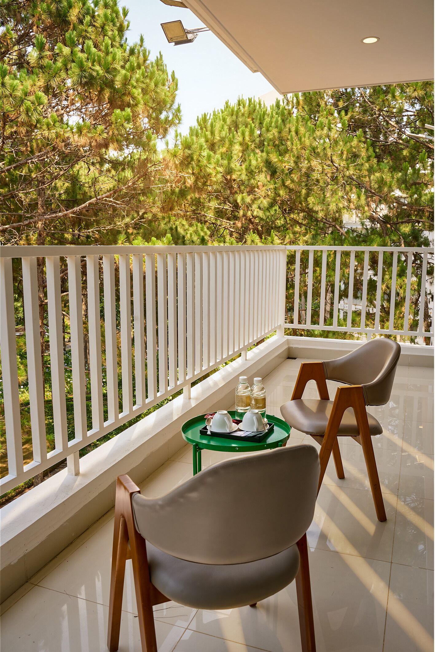 A balcony with two chairs, a small table with a tray, and a view of pine trees.