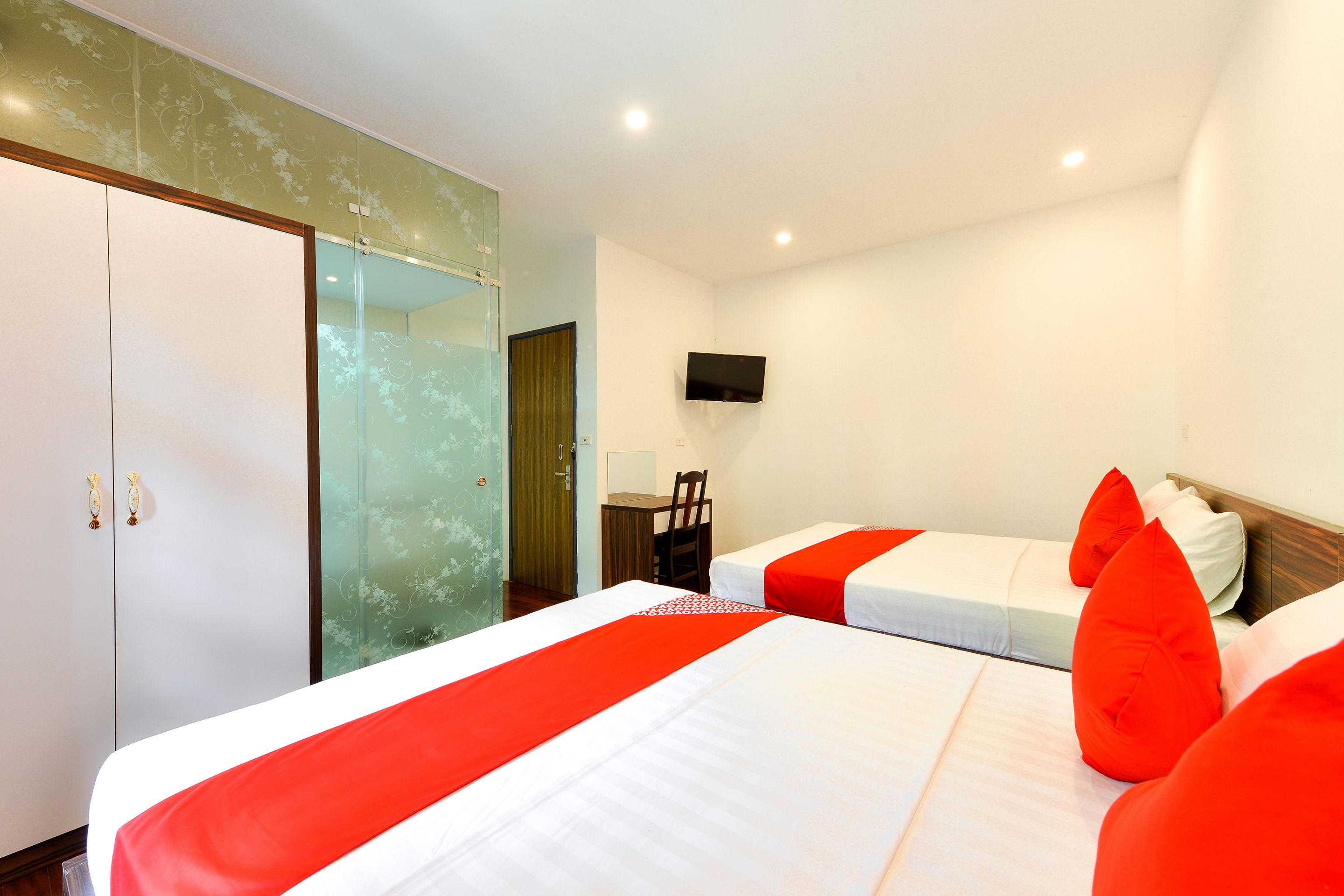 Une chambre d’hôtel avec deux lits, un bureau, une chaise et un téléviseur fixé au mur.