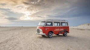 A vintage red van parked on a sandy beach with a cloudy sky. - Kajüte Sieben 2 (St. Peter-Ording)