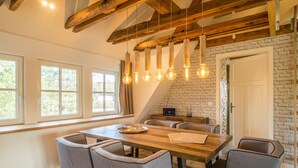 A dining area with a wooden table and grey upholstered chairs, a brick wall, and exposed wooden beams. - Kajüte Sieben 2 (St. Peter-Ording)
