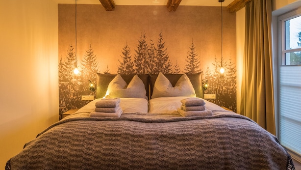 A bedroom with a large bed, wooden beams on the ceiling, and a window with curtains. - Kajüte Sieben 2 (St. Peter-Ording)