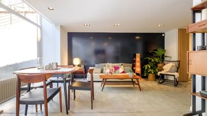 Uma sala de estar moderna com área de jantar, apresentando um sofá, cadeiras, uma mesa de centro e uma estante.