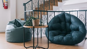 Un interior moderno con una escalera de madera, baranda de metal negro, un sillón informal negro, una pequeña mesa con una planta y un extintor en la pared.