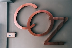 A wall with large, metallic letters spelling "COZ" and a small, rectangular object with a logo. - COZ at Ratchathewi - Hostel (Bangkok)