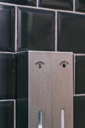 Two metallic dispensers labeled "SHAMPOO" and "SHOWER GEL" mounted on a tiled wall. - COZ at Ratchathewi - Hostel (Bangkok)