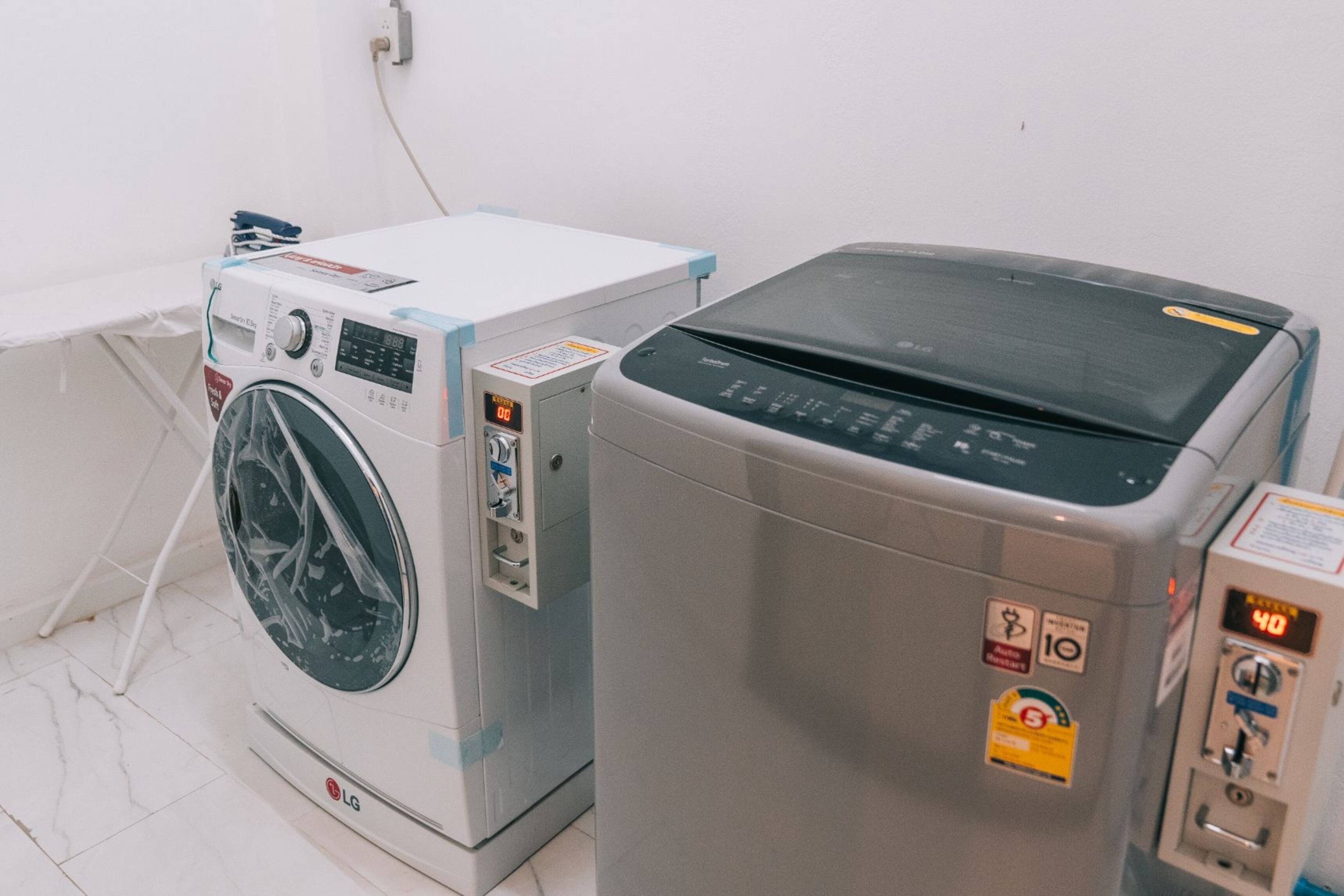 Two washing machines side by side in a room with white walls and a tiled floor.