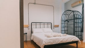 Una cama bien hecha con sábanas blancas, cabecera de metal negro y suelo de madera.