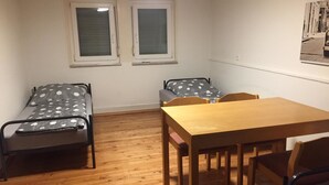 A small, sparsely furnished room with two beds, a wooden table, and a chair. - Pfaffenhofen Monteurzimmer (Pfaffenhofen)