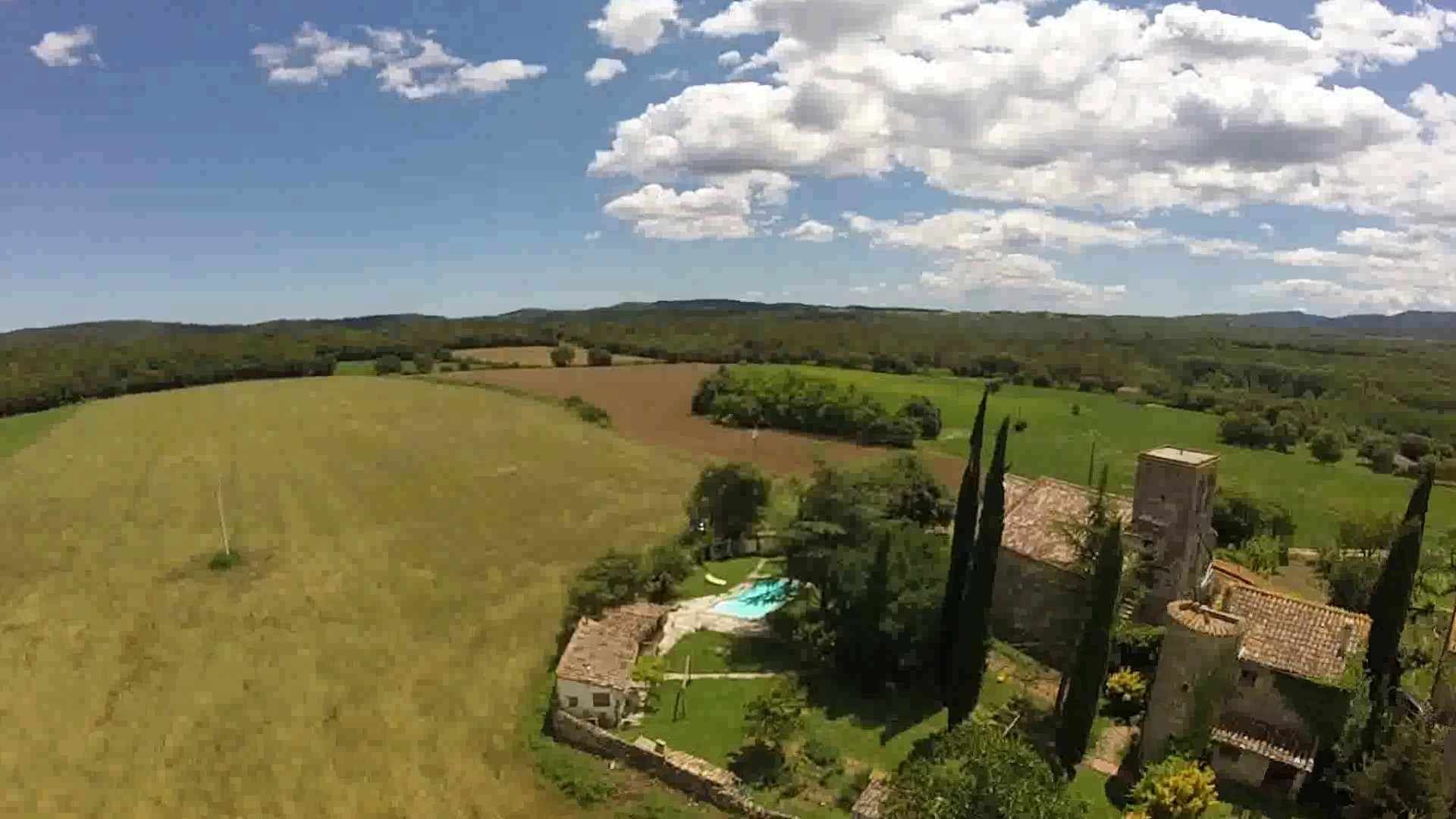 Paisaje rural con un extenso campo abierto, un edificio pequeño y una piscina, y algunos árboles altos.