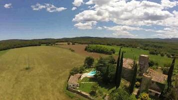 Paisaje rural con un extenso campo abierto, un edificio pequeño y una piscina, y algunos árboles altos.