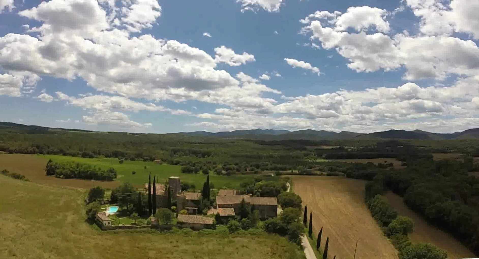 Un paisaje rural con un pequeño conjunto de edificios tradicionales rodeado de campos y árboles, bajo un cielo parcialmente nublado.