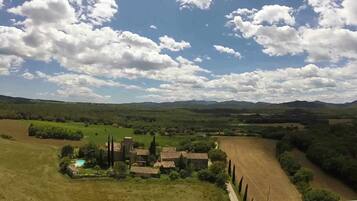 Un paisaje rural con un pequeño conjunto de edificios tradicionales rodeado de campos y árboles, bajo un cielo parcialmente nublado.