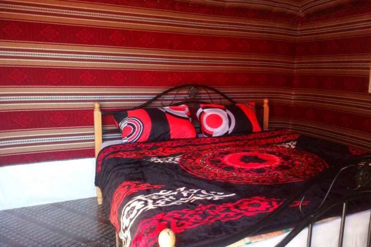 A room with a bed, striped wallpaper, and a red and black patterned bedspread.
