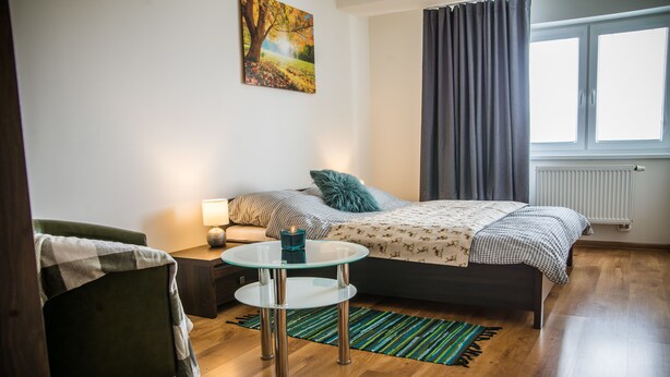 A modern bedroom with a bed, a chair, a small table, and a window with curtains. - Apartment Eric 9D High Tatras (Velky Slavkov)