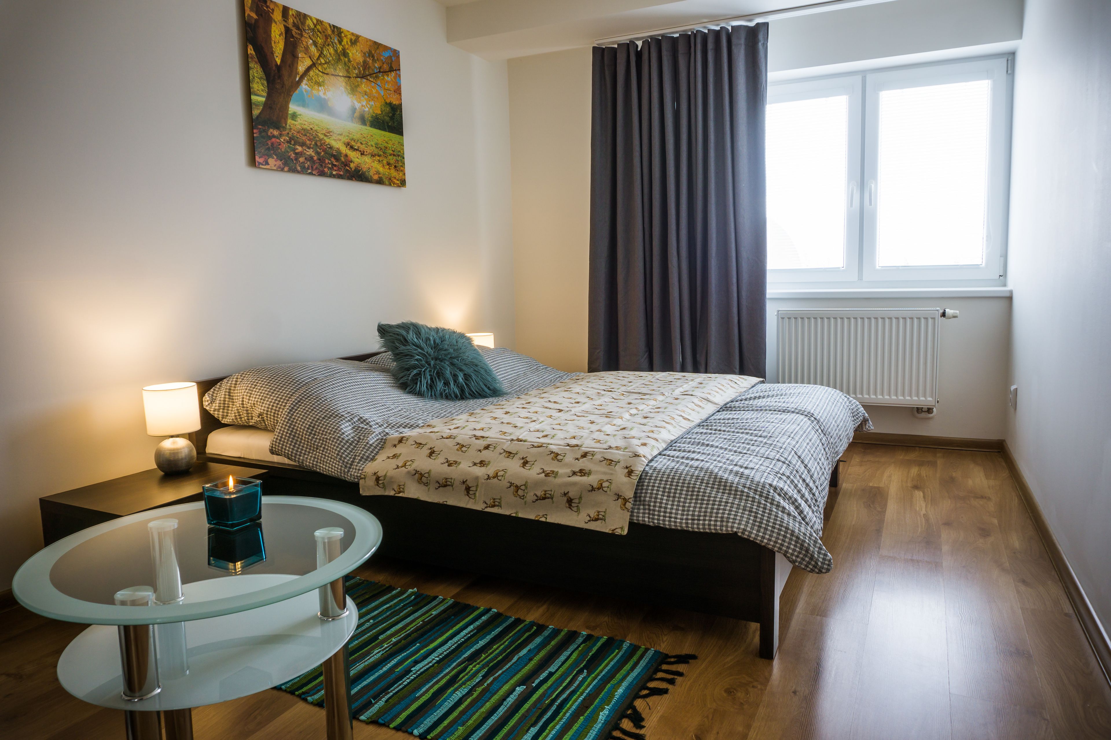 A bedroom with a bed, bedside table, lamp, and a view of the outdoors through a window.
