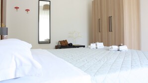 Habitación de hotel con una cama grande, un armario, un espejo y una mesita de noche con una lámpara y una planta decorativa.