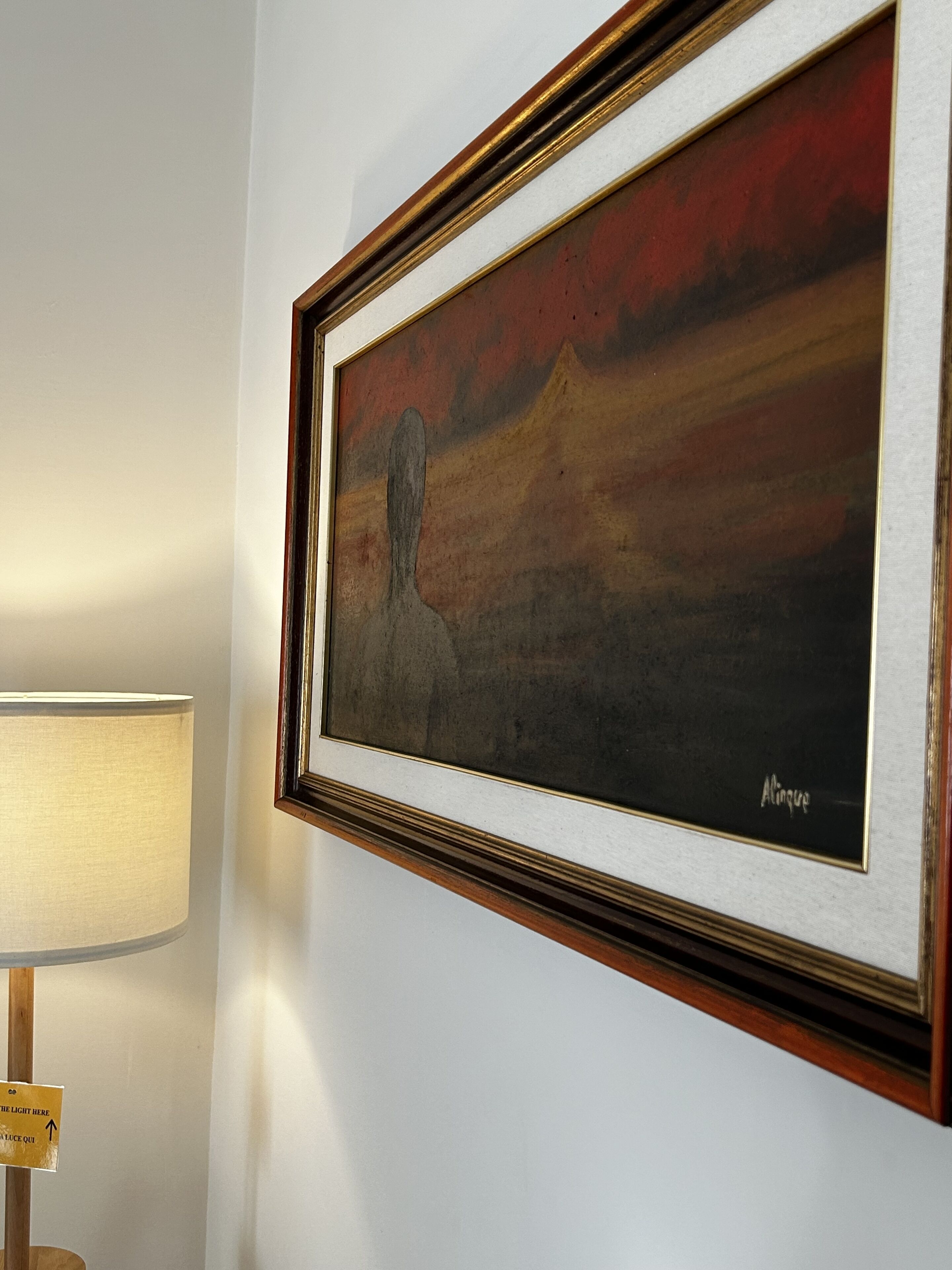 A framed painting on a wall, a lamp, and a sign with arrows.