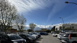 Un estacionamiento con varios coches aparcados en espacios designados, cielo despejado y edificios al fondo.