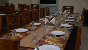 Uma longa mesa de jantar posta com pratos, copos e talheres, rodeada por cadeiras de madeira.