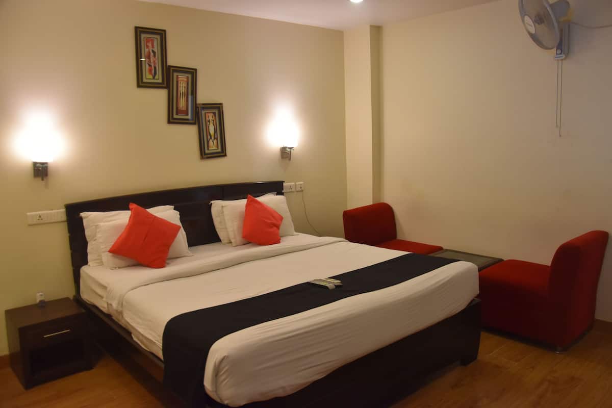 Une chambre d’hôtel avec un grand lit, deux tables de chevet, un bureau et deux chaises rouges.