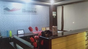 Uma receção com uma placa a indicar "Hotel CORPORATE INN", um certificado emoldurado e um vaso com flores vermelhas.