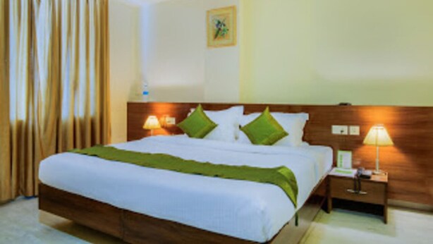 Quarto de hotel com cama grande, cabeceira de madeira, duas luminárias de cabeceira e mesa de apoio.