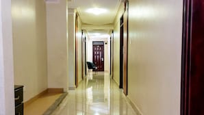 A hotel corridor with a tiled floor, wooden doors, and a chair in the distance. - Fancy Hotel (Kampala)