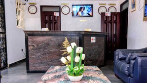 A reception area with a marble reception desk, a blue sofa, and a floral centerpiece on a patterned table. - Fancy Hotel (Kampala)