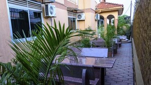 A narrow outdoor patio with a stone bench, potted plants, and a building with air conditioning units. - Fancy Hotel (Kampala)