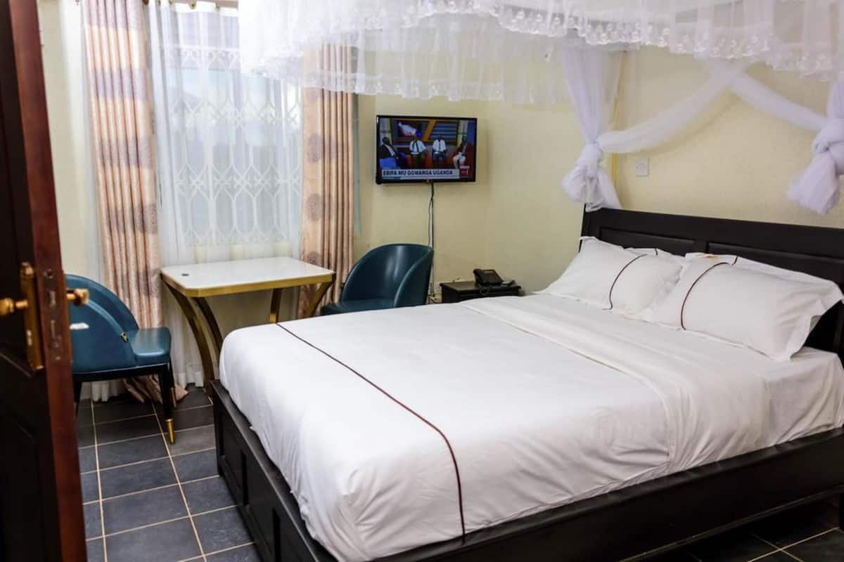 Quarto de hotel com uma cama, uma escrivaninha, uma cadeira e televisão na parede.