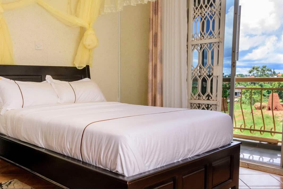 Uma cama com roupa de cama branca, cabeceira escura e vista para um jardim através de uma janela com ferro ornamental.